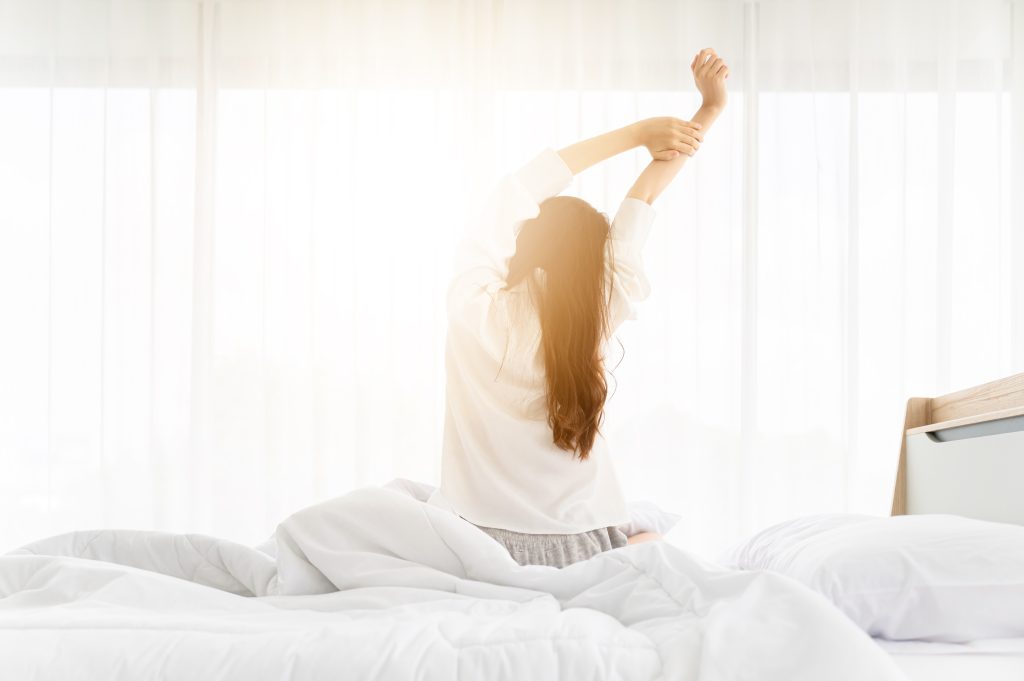 woman stretches sitting on bed besides window
